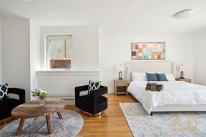 A modern bedroom with a large bed, two nightstands, a wooden coffee table, and two chairs. - Luxury PH Duplex w/Private Terrace by Central Park (New York)