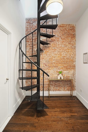 A spiral staircase with a brick wall backdrop, a small console table with a vase, and a wooden floor. - Luxury PH Duplex w/Private Terrace by Central Park (New York)