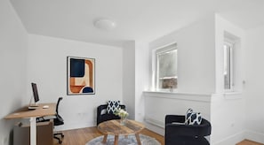 A modern living room with a wooden desk, a round coffee table, two black armchairs, a large abstract painting, and a window with a view of a brick wall. - Luxury PH Duplex w/Private Terrace by Central Park (New York)