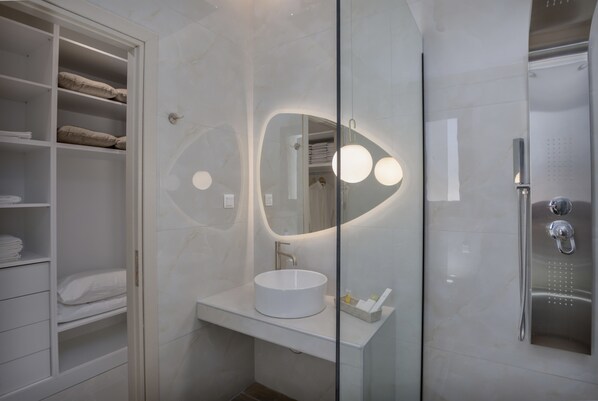 Un baño moderno con un lavamanos redondo, una cabina de ducha con mampara de vidrio y un mueble de almacenamiento empotrado.