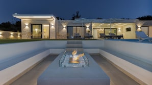 A modern outdoor patio with a built-in fire feature, seating, and a pool.