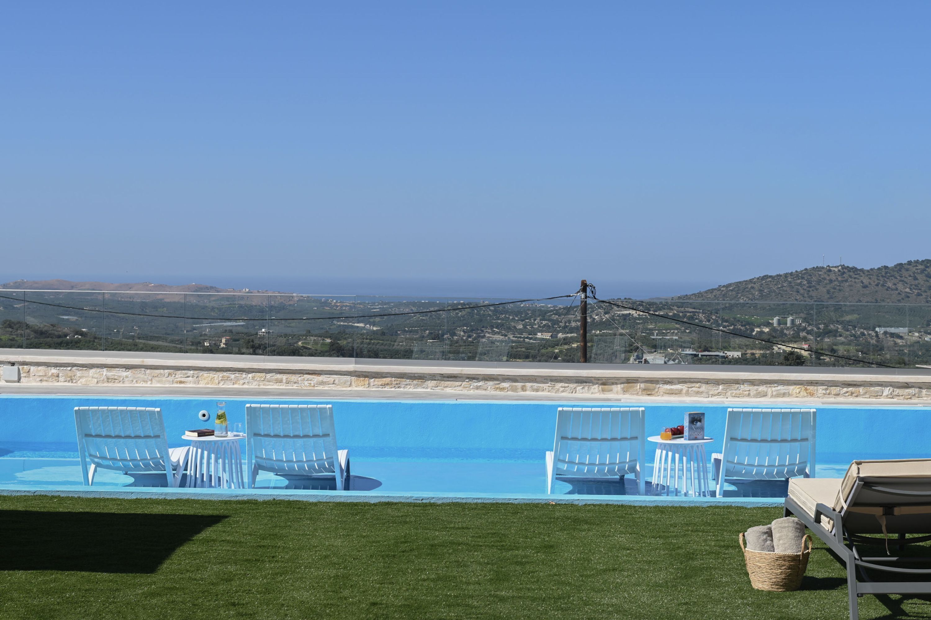 A swimming pool with lounge chairs and a table, overlooking a scenic landscape.