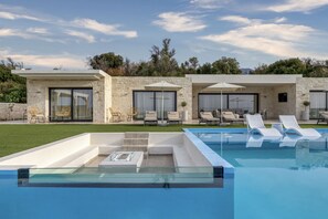 Un área de piscina moderna con sillones de descanso y un jacuzzi con paredes de vidrio.