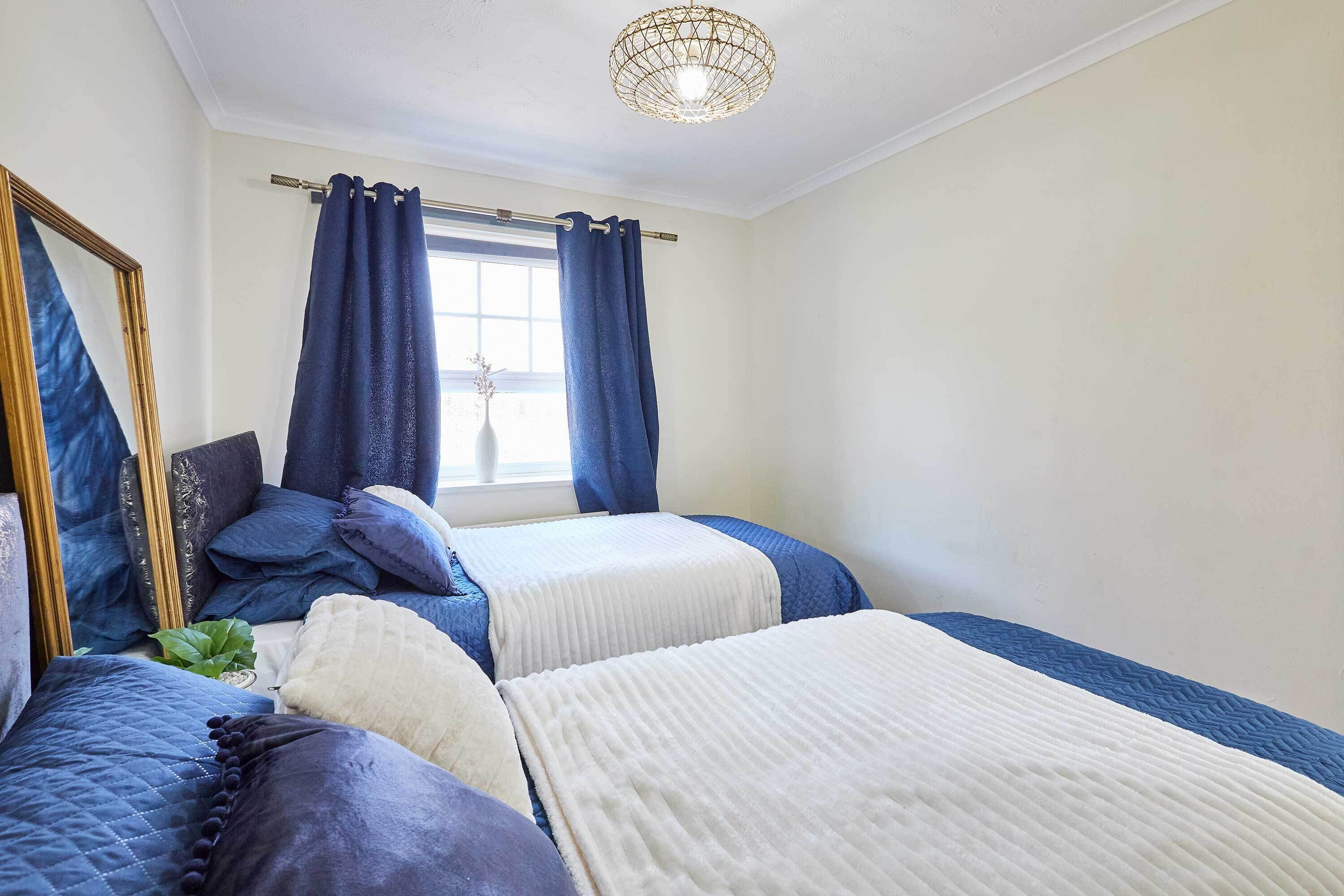 A bedroom with two beds, a large mirror, and a window with curtains.