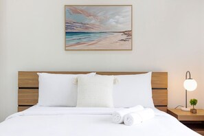 A neatly made bed with white linens and a beach-themed painting above it. - Zen Coastal Hideaway Modern Hospital Beach (Darwin)