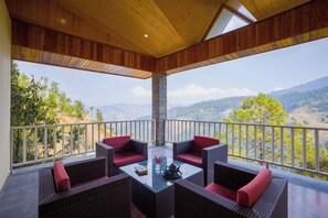 A balcony with wicker furniture and a glass table, overlooking a mountainous landscape. - Alaya Stays Luuma Luxury Villa - Hillside 5-BHK Villa Amidst Pines With Garden, Balcony & Lounge (Shimla)