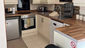 A compact kitchen with white cabinets, a microwave, a toaster, a sink, and a trash bin. - Fabulous Open Views Over Dufftown (Keith)