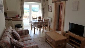 A cozy living room with a sofa, a coffee table, a TV, and a dining area with a table and chairs. - Fabulous Open Views Over Dufftown (Keith)