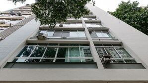 A multi-story building with large windows, air conditioning units, and a tree partially obscuring the view. - Rj04 Ap em Copacabana até 6 pessoas (Rio de Janeiro)