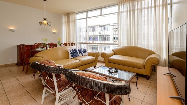 A living room with two sofas, a coffee table, wicker chairs, a dining table, and a chandelier. - Rj04 Ap em Copacabana até 6 pessoas (Rio de Janeiro)