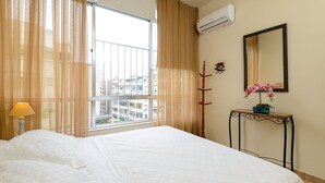 A hotel room with a large bed, a window with sheer curtains, a bedside table with a lamp, and a mirror on the wall. - Rj04 Ap em Copacabana até 6 pessoas (Rio de Janeiro)