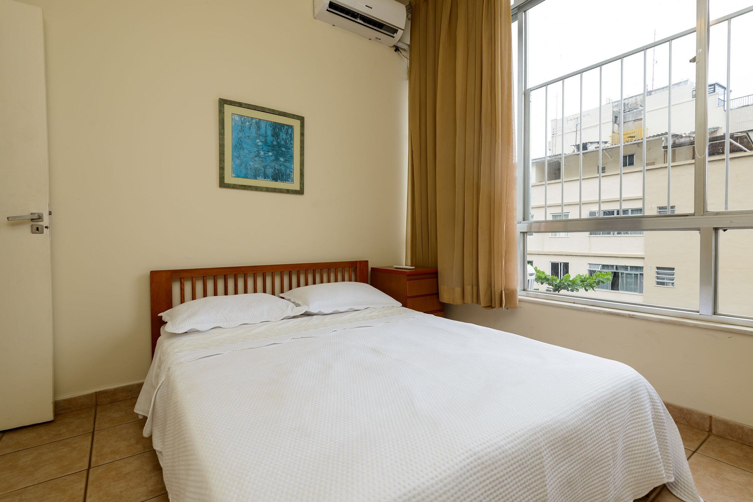 Ein Hotelzimmer mit Bett, Nachttisch, einem Fenster mit Vorhängen und einer Wand-Klimaanlage.