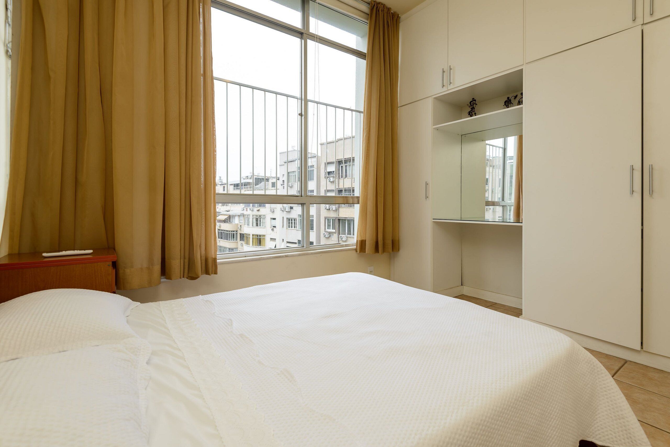 Una habitación de hotel con una cama grande, una ventana con cortinas, un armario y una mesita con un control remoto.