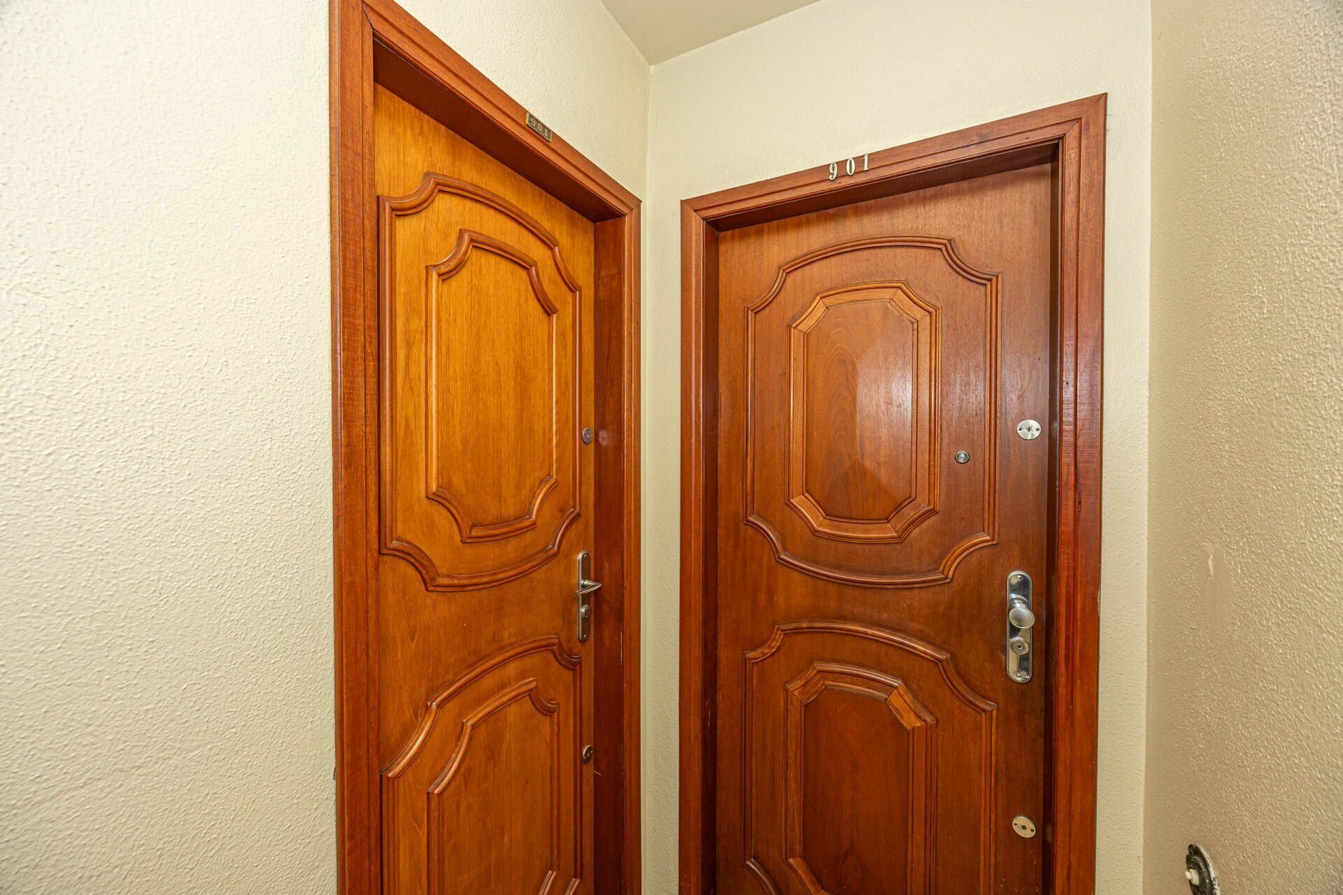 Two wooden doors with a classic design, each with a doorbell and a lock.