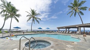 A pool area with lounge chairs and umbrellas, a hot tub, and palm trees. - Big Island Kanaloa At Kona 2802 2 Bedroom Condo (Kailua-Kona)