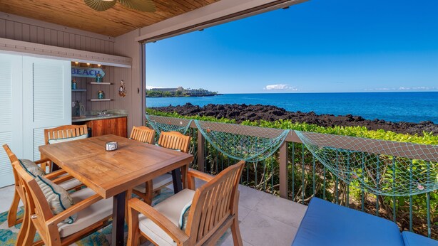 A wooden dining table with chairs, a view of the ocean, and a hammock. - Big Island Kanaloa At Kona 2802 2 Bedroom Condo (Kailua-Kona)