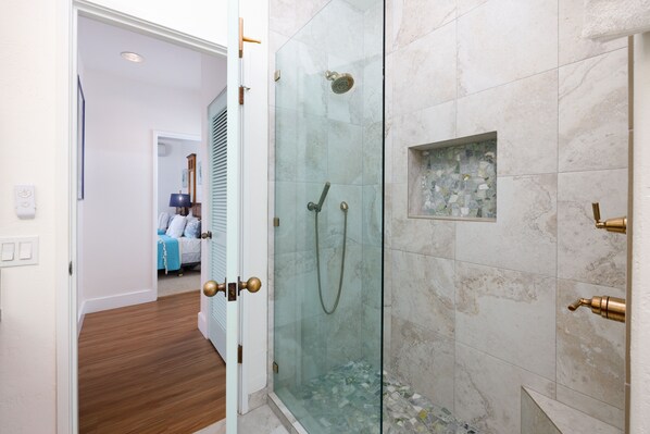 Un baño moderno con ducha de vidrio, baldosas de mármol y suelo de madera.