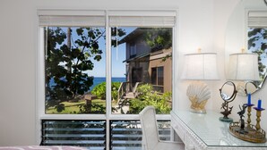 A room with a large window, a wicker desk, a chair, and a bed with a pink and white patterned bedspread. - Big Island Kanaloa At Kona 2802 2 Bedroom Condo (Kailua-Kona)