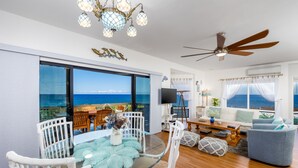 A modern living room with a glass table, white wicker chairs, a ceiling fan, and a view of the ocean. - Big Island Kanaloa At Kona 2802 2 Bedroom Condo (Kailua-Kona)