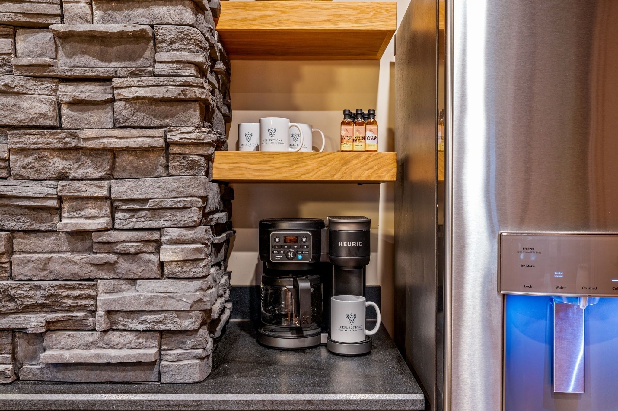 A kitchenette with a stone wall, a coffee maker, a mug, and a shelf with coffee bottles.