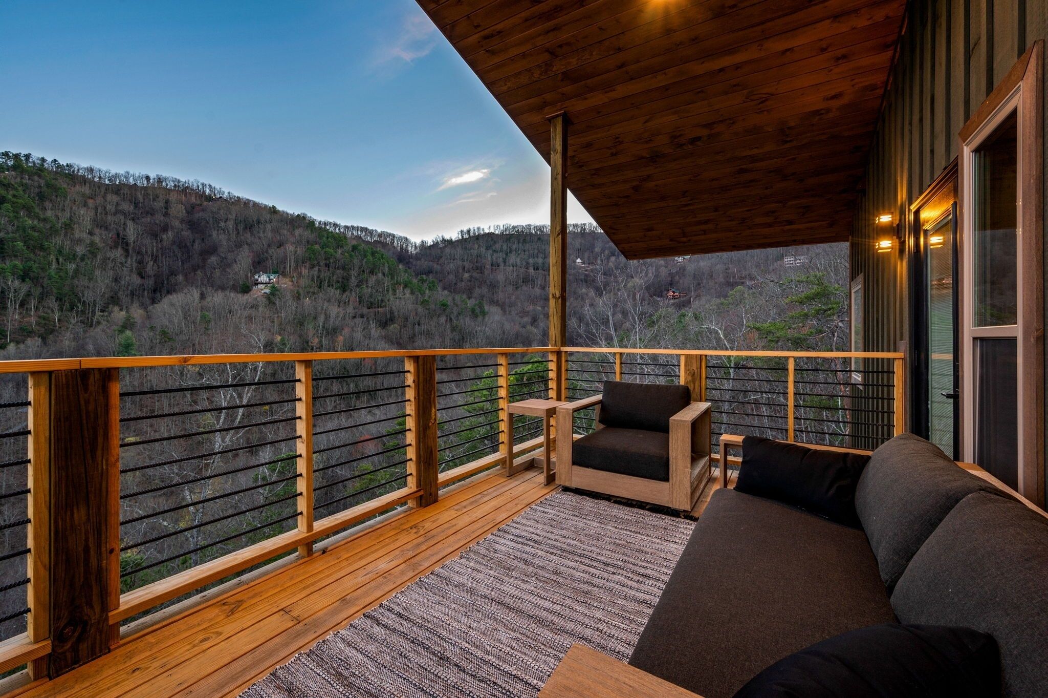 A wooden deck with a sofa and chairs, overlooking a forested hillside.