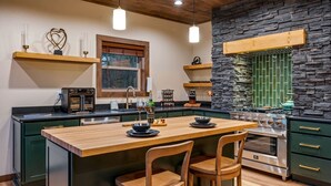 A modern kitchen with a central island, wooden chairs, a built-in oven, and stone accents. - Reflections 1 Bedroom Cabin (Sevierville)