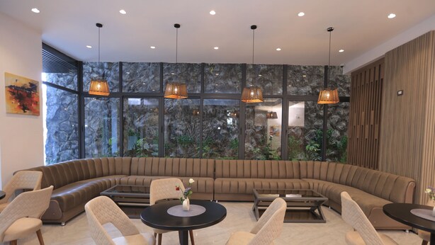 A modern lounge area with a large curved sofa, round tables, and chairs, featuring a large window with a view of greenery. - Daylin Guest House (Addis Ababa)