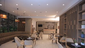 A modern interior with a seating area, tables, and a kitchen in the background. - Daylin Guest House (Addis Ababa)