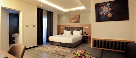 A modern hotel room with a large bed, a desk, a sofa, and a dining area.
