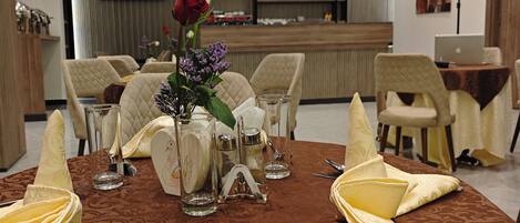 A dining table set with a vase of flowers, salt and pepper shakers, and a napkin folded in a fan shape.