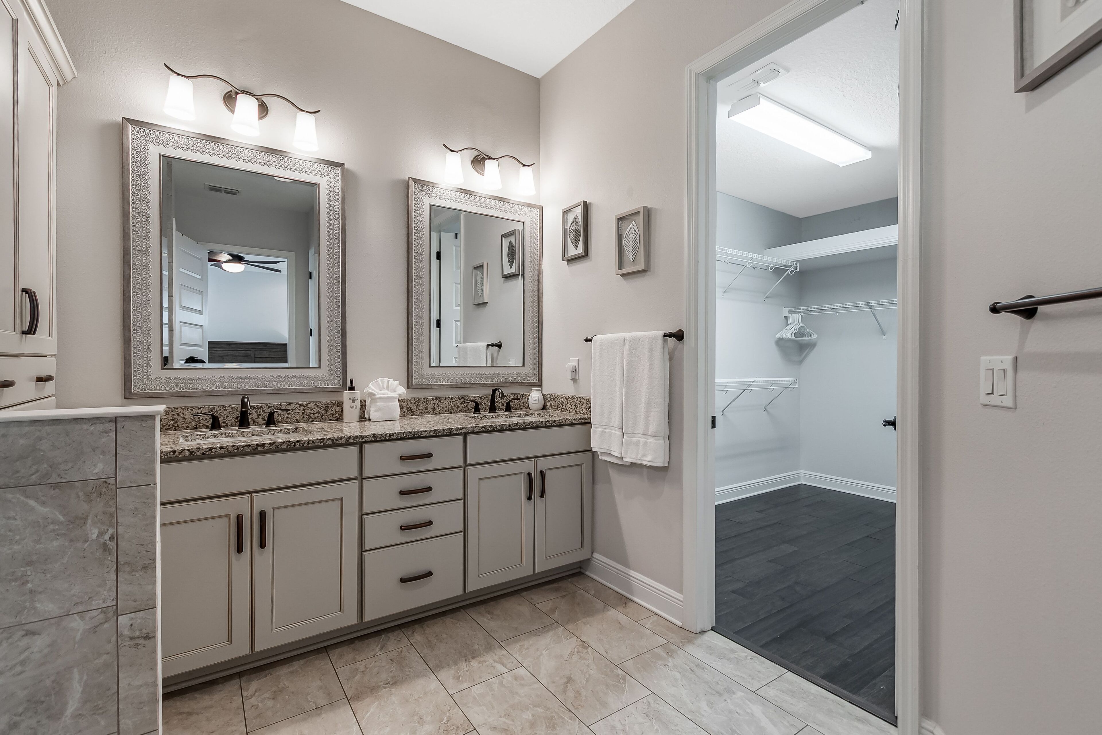 A modern bathroom with two large mirrors, a vanity with a granite countertop, and a walk-in shower.
