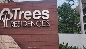 A sign for Trees Residences with a modern design and a logo featuring stylized trees.