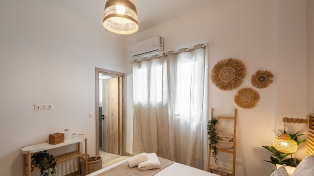 A bedroom with a bed, a bedside table, a chair, a hanging light, and a wall-mounted air conditioner. - LIV - Seaside Getaway in Glyfada (Glyfada)