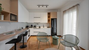 A modern kitchen with a wooden countertop, black bar stools, and a green chair. - LIV - Seaside Getaway in Glyfada (Glyfada)