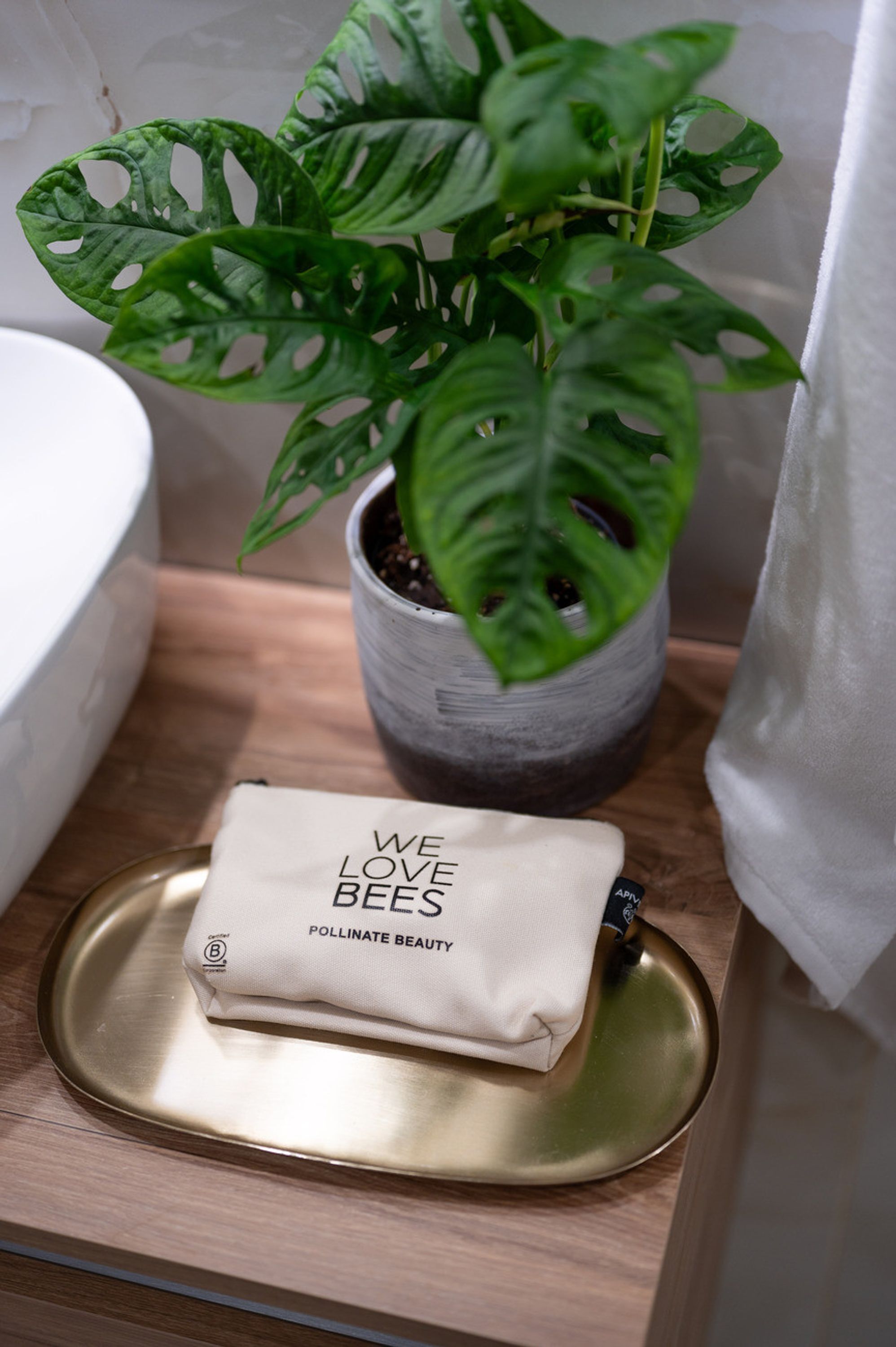 A bathroom with a potted plant, a white sink, and a tray with a bees-themed pouch.