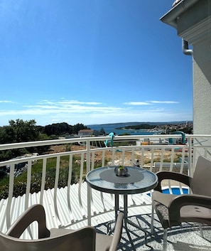 A balcony with a table and chairs, overlooking a coastal view with buildings and a clear sky. - Apartment Rosmarin nr. 2 in the Town of Krk with Sea and Old Town Views, Close to the Beach (Krk)