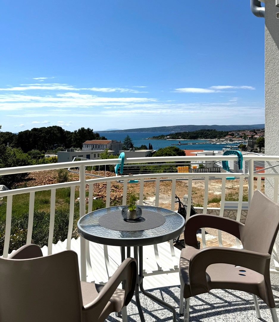 A balcony with a table and chairs, overlooking a coastal view with houses and a body of water.