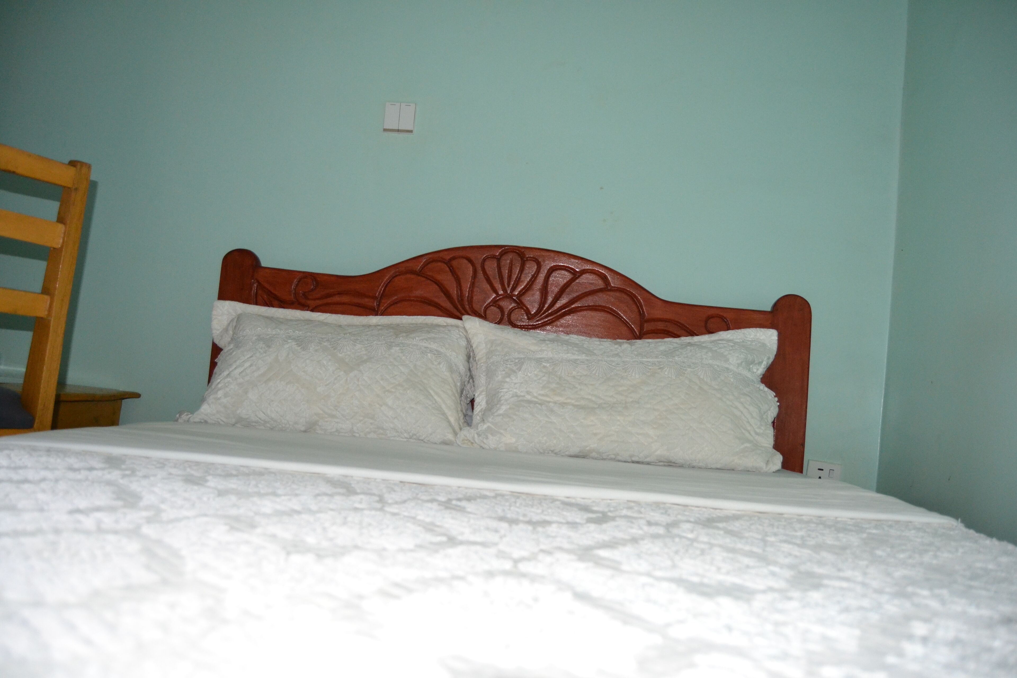 Una cama con cabecera de madera, dos almohadas y una colcha blanca en una habitación con paredes azul claro.