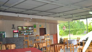 Une chambre d’hôtel avec un lit, un coin bar avec des étagères remplies de bouteilles, et une vue sur la verdure à l’extérieur.