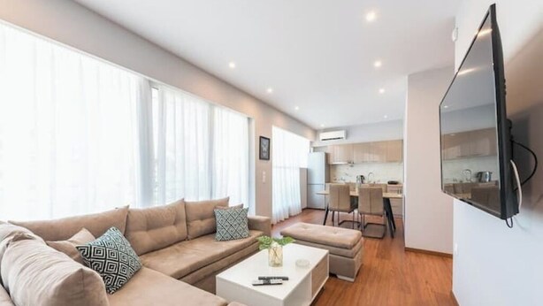 A modern living room with a beige sofa set, a white coffee table, and a flat-screen TV mounted on the wall.