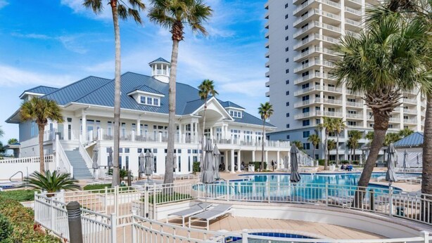 Un resort con una amplia zona de piscina, un edificio imponente con balcón corrido y palmeras.