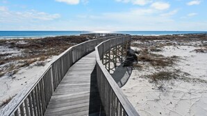 Un paseo marítimo de madera que lleva a una playa con cielo despejado.
