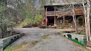 A two-story cabin with a stone exterior, a balcony, and a gravel driveway.