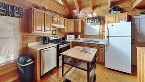 A wooden cabin kitchen with a stove, sink, refrigerator, and a small table with a cart.