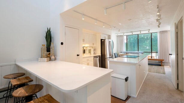A modern kitchen with white countertops, wooden stools, and a large island. - Updated Park City 2BR Sleeps 7-Natural Light & A/C-Walk to Park City Resort (Park City)