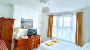 Une chambre d’hôtel avec un lit, une commode en bois, un téléviseur et un tableau accroché au mur.