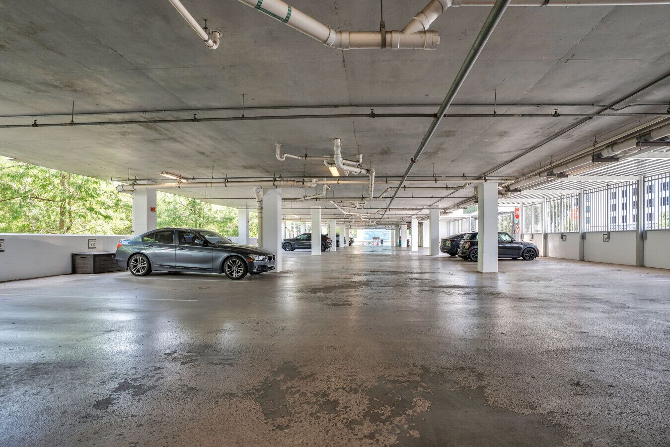 Un estacionamiento subterráneo con pilares de concreto, piso mojado y automóviles estacionados.