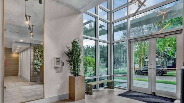 A modern lobby with large windows, a wooden bench, and a potted plant. - Luxurious 2/2 Downtown Apartment (Orlando)