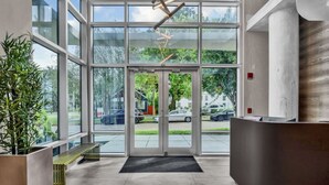 A reception area with a glass door entrance, a reception desk, a bench, and a potted plant. - Luxurious 2/2 Downtown Apartment (Orlando)