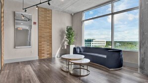 A modern office space with a large window, a round table, a blue sofa, and a wooden accent wall. - Luxurious 2/2 Downtown Apartment (Orlando)